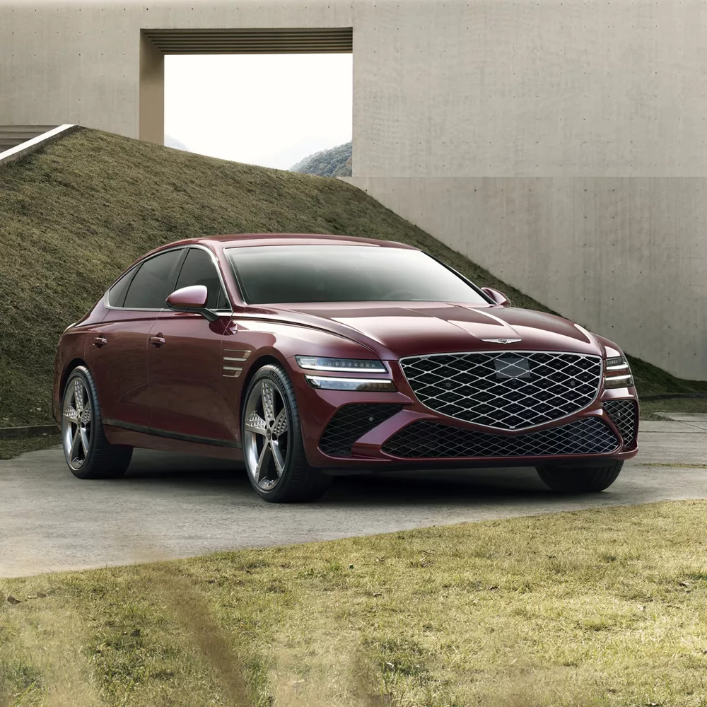 3/4 front passenger side angle of Genesis G80 in Cavendish Red parked in front of modern house