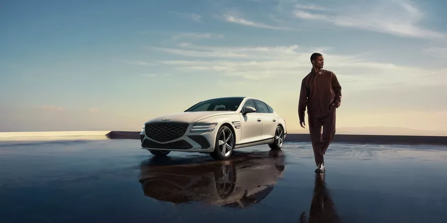 Man walking next to Genesis G80 in Uyuni White on reflective terrace at sunset