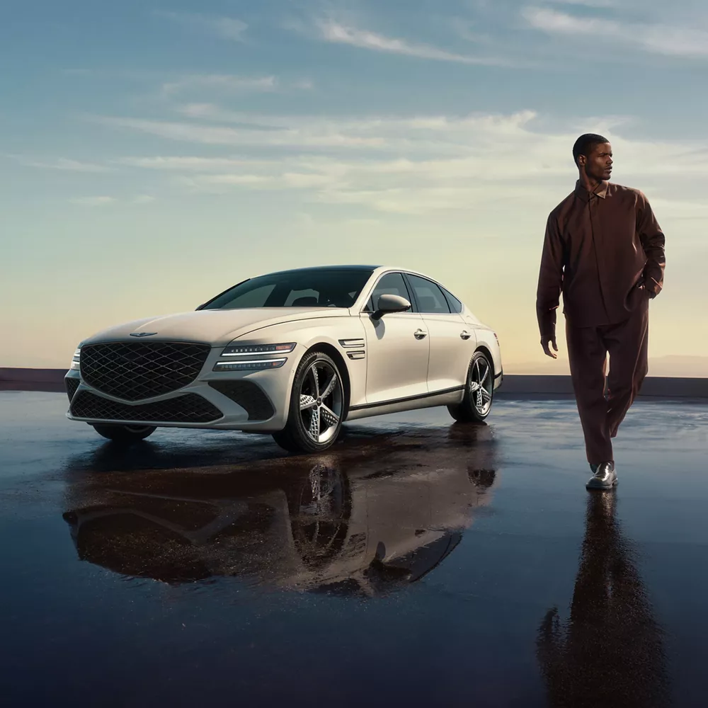 3/4 front driver side view of Genesis G80 in Vatna Gray parked on reflective surface as man walks by