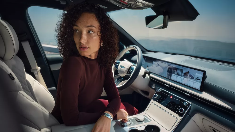 Interior passenger side view of woman sitting in driver seat looking toward rear of Genesis G80