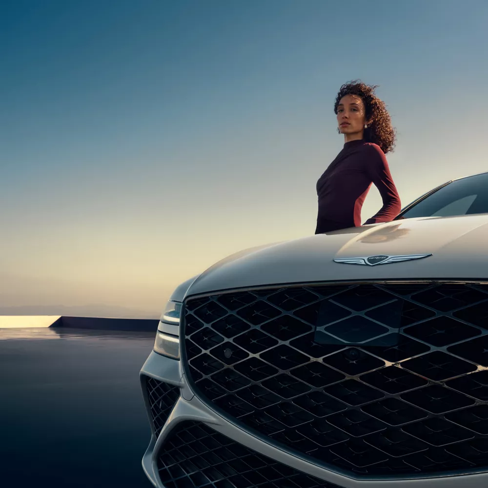 Genesis G80 in Uyuni White with bold crest grille on reflective terrace at sunset