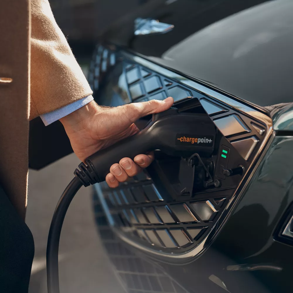 Close up of a hand holding an electric charger to the grill of a Genesis Electrified G80