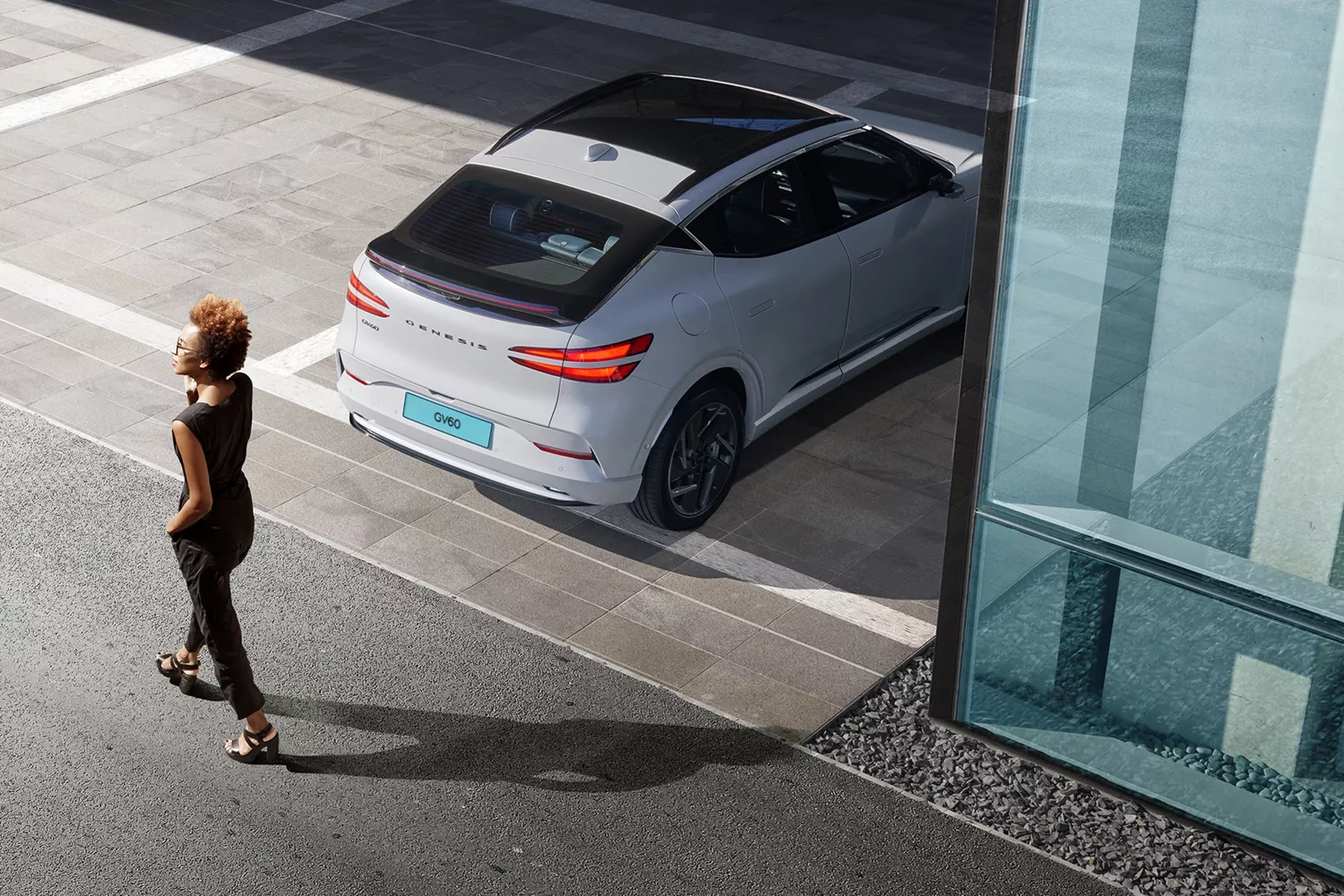 Rear view of Genesis GV60 parked as woman walks behind, highlighting rear collision avoidance feature