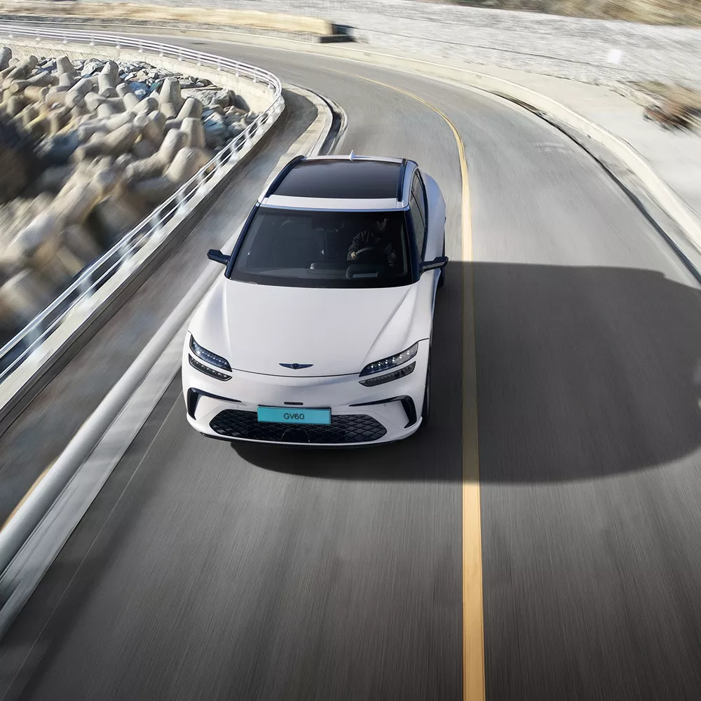 Front aerial view of 2026 Genesis GV60 in white driving on coastal road