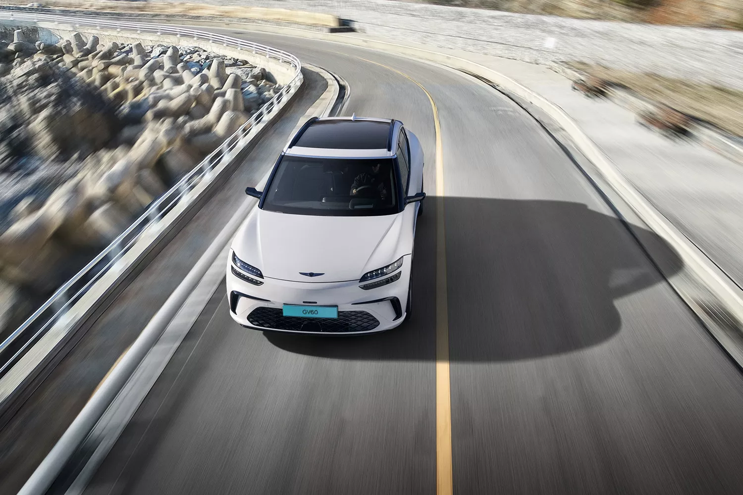 Front aerial view of 2026 Genesis GV60 in white driving on coastal road