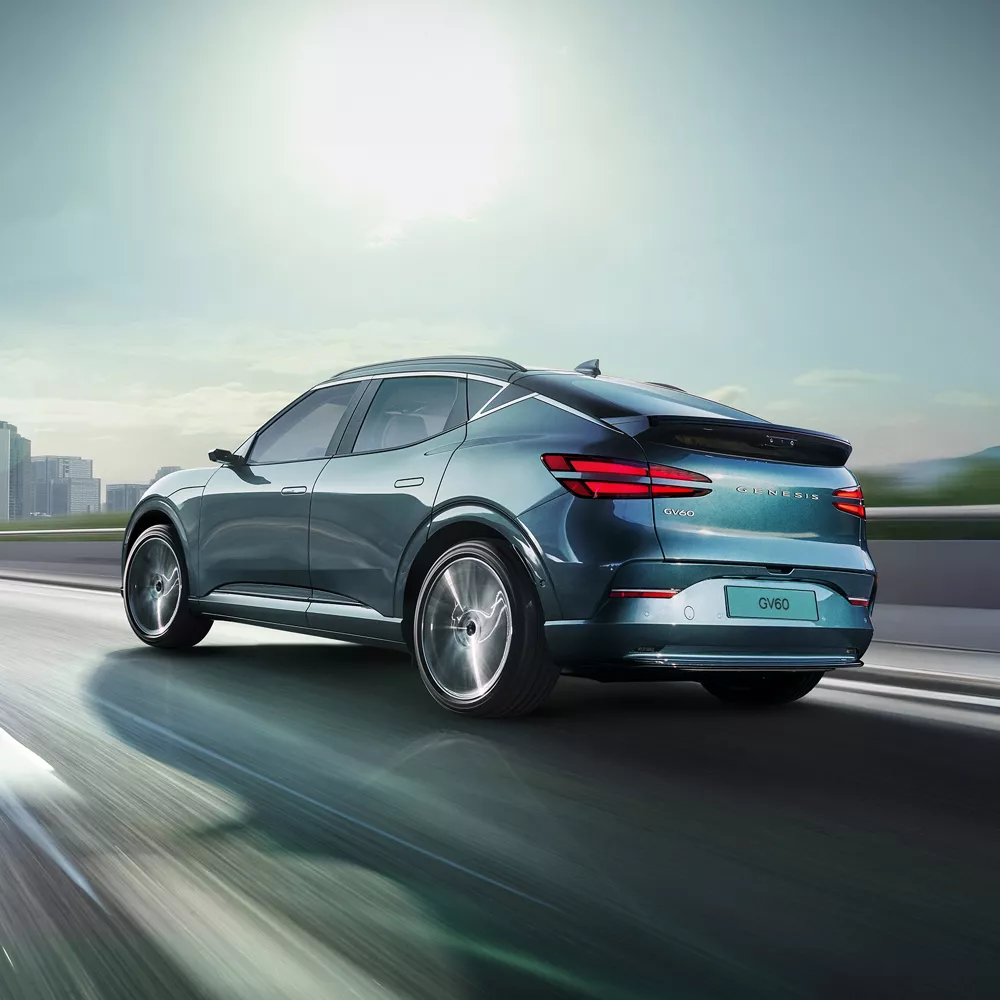 3/4 rear driver side view of 2026 Genesis GV60 in Tromso Green driving on city skyline highway