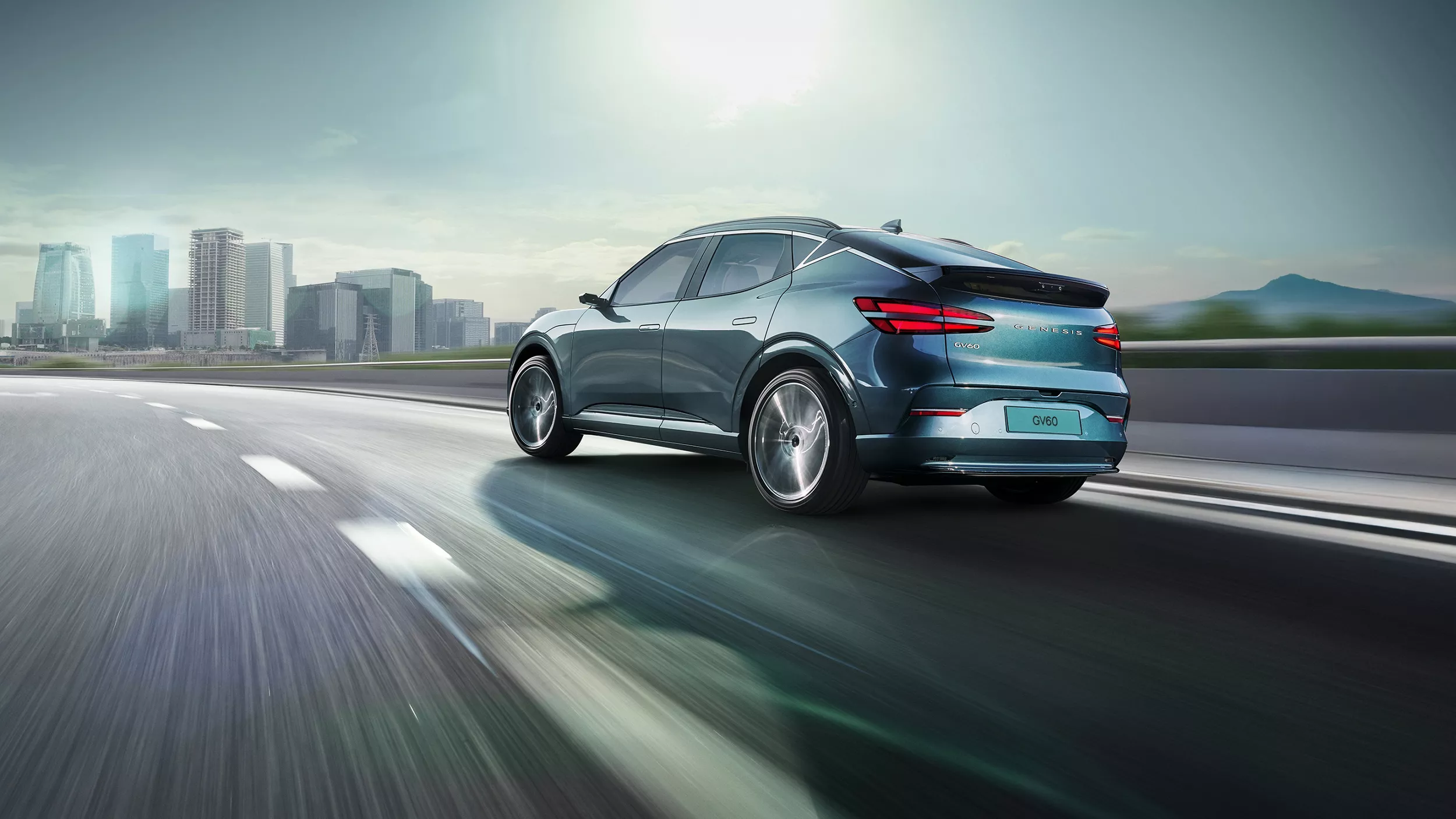 3/4 rear driver side view of 2026 Genesis GV60 in Tromso Green driving on city skyline highway