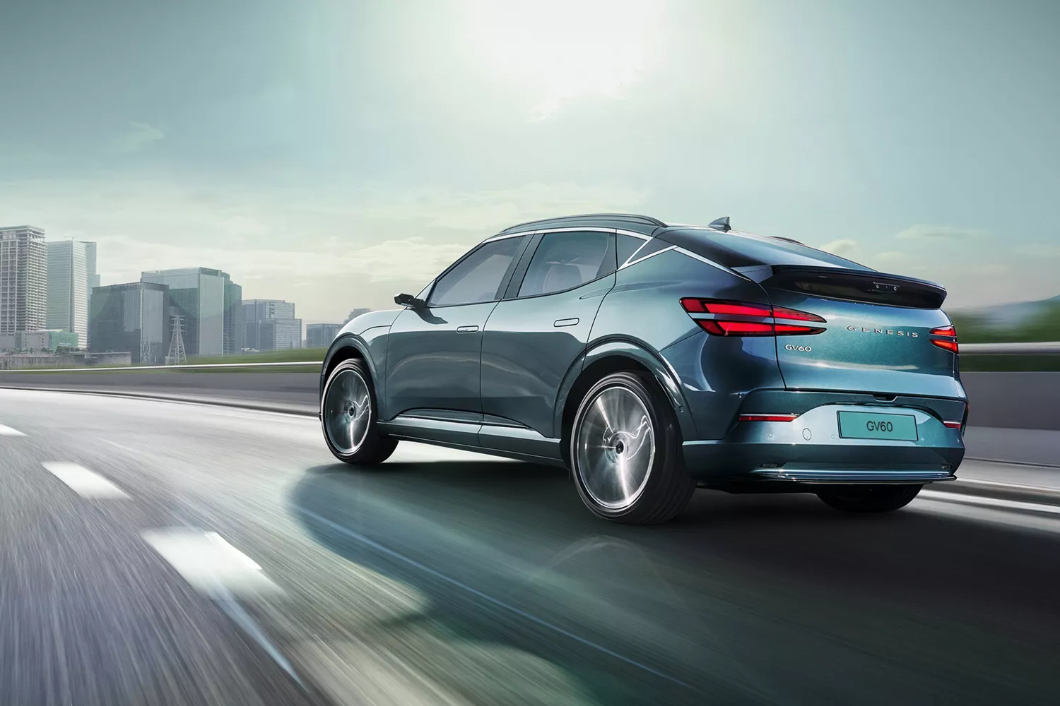 3/4 rear driver side view of 2026 Genesis GV60 in Tromso Green driving on city skyline highway