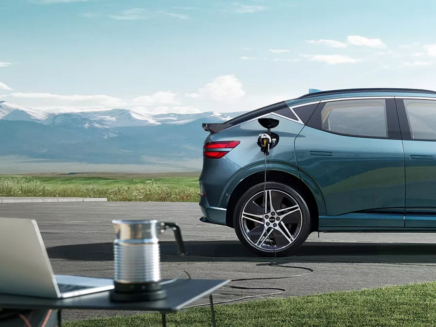 2026 Genesis GV60 in Tromso Green charging with mountain backdrop and clear sky scenery