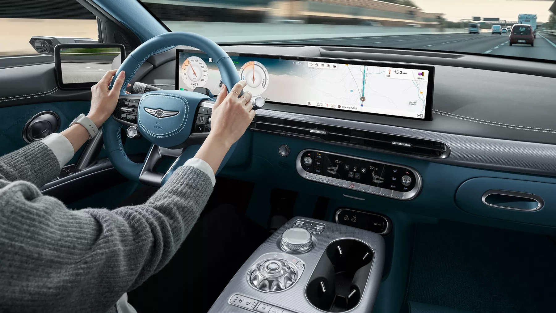 2026 Genesis GV60 interior from driver’s view with blue wheel, digital dash, and highway ahead