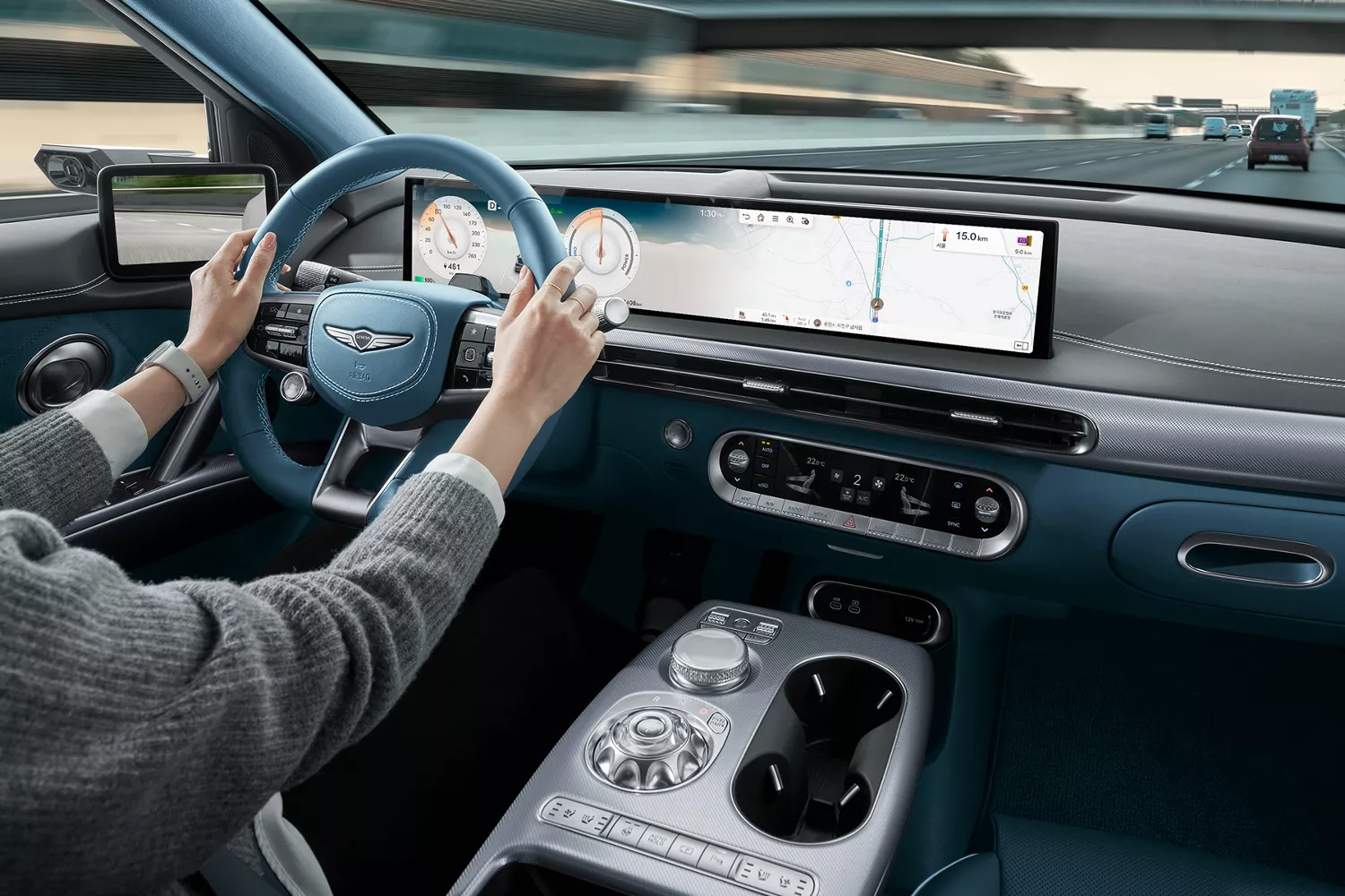 2026 Genesis GV60 interior from driver’s view with blue wheel, digital dash, and highway ahead