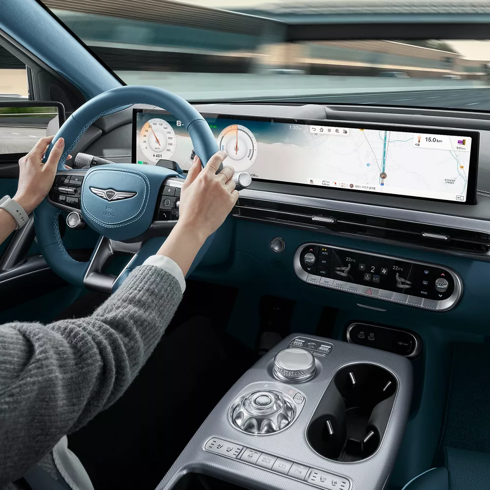 2026 Genesis GV60 interior from driver’s view with blue wheel, digital dash, and highway ahead