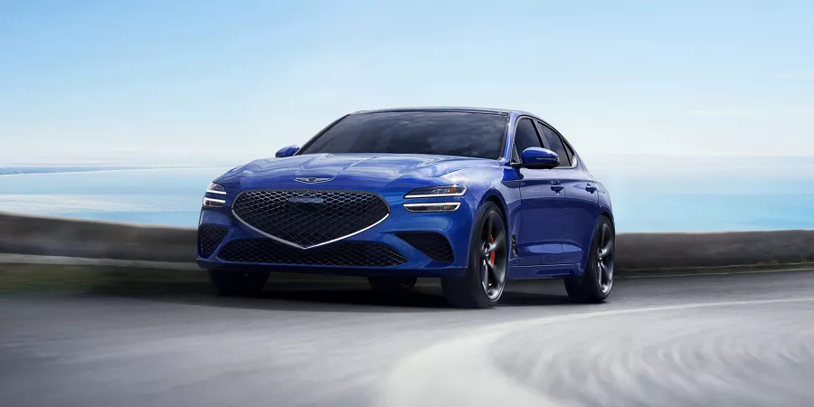 Front driver side action shot of Genesis G70 in Kawah Blue driving on a coastal highway