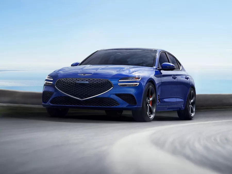 Front driver side action shot of Genesis G70 in Kawah Blue driving on a coastal highway