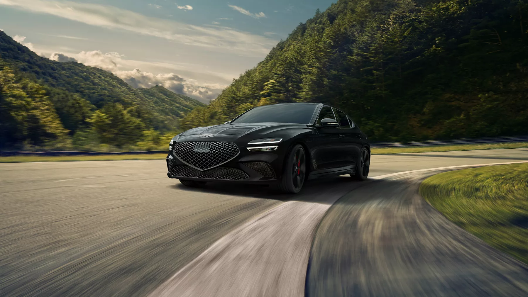 3/4 driver side profile view of Genesis G70 in Vik Black driving on a road through hilly backdrop