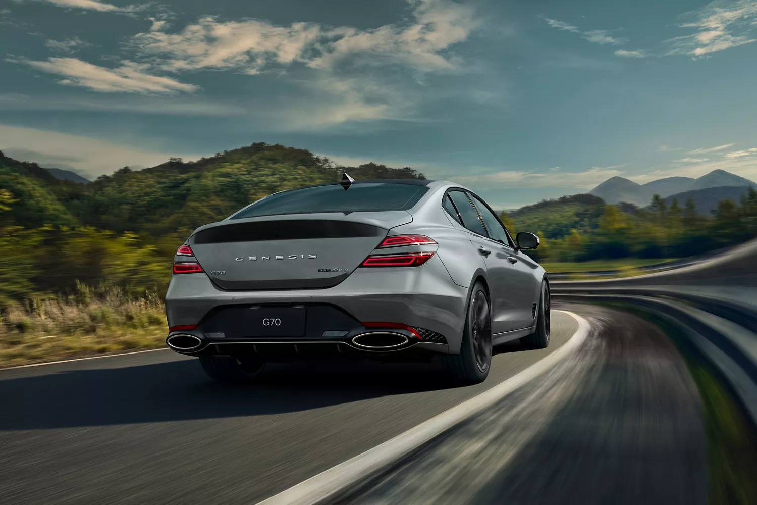 3/4 rear passenger side view of Savile Silver Genesis G70 on highway with mountains in background