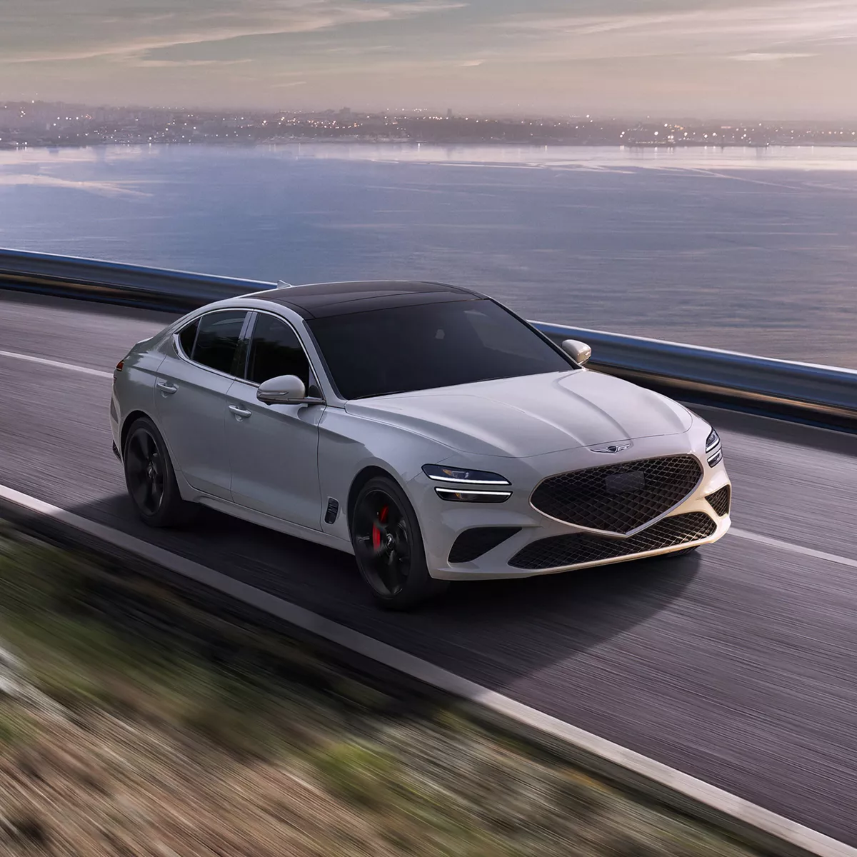 3/4 front passenger side angle of Genesis G70 in Bond Silver driving on coastal road at daytime