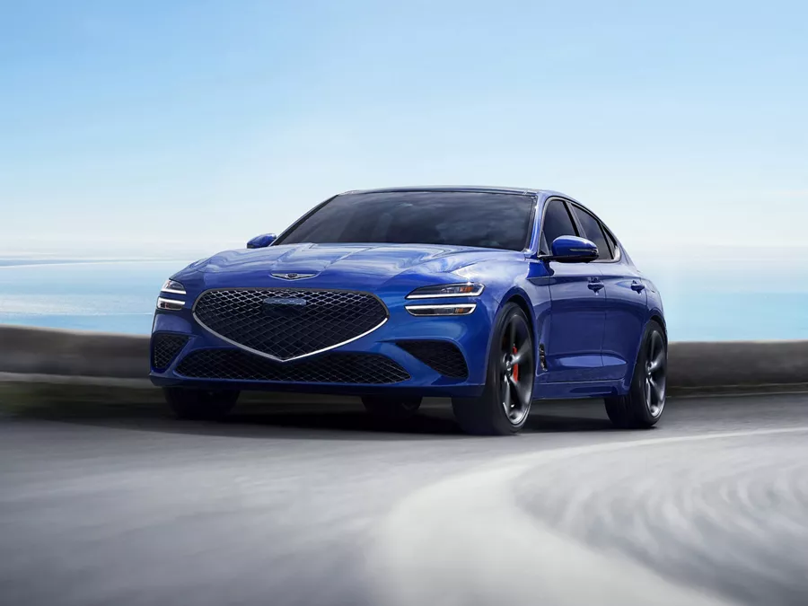 Front driver side action shot of Genesis G70 in Kawah Blue driving on a coastal highway