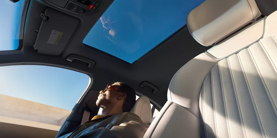 Interior view from empty driver's seat of passenger sitting beneath open sunroof inside Genesis G70