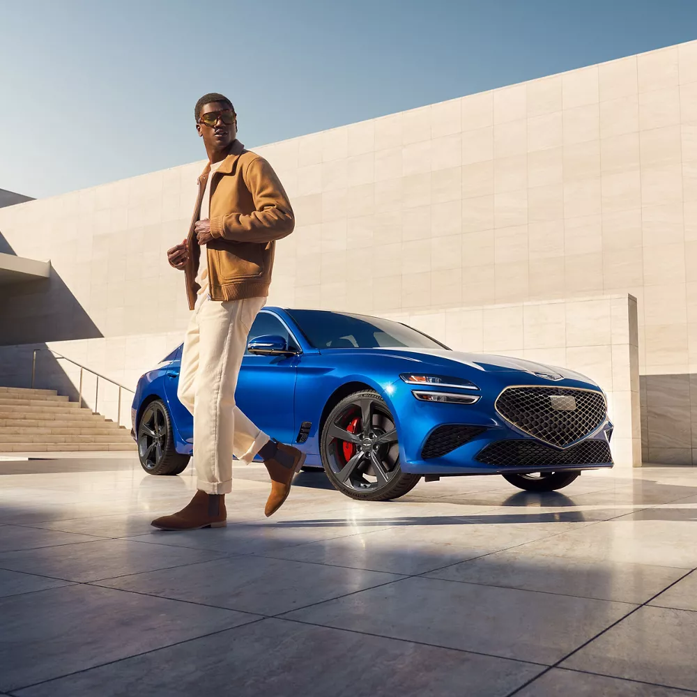 Passenger side view Genesis G70 in Kawah Blue parked on rooftop with man walking in forefront