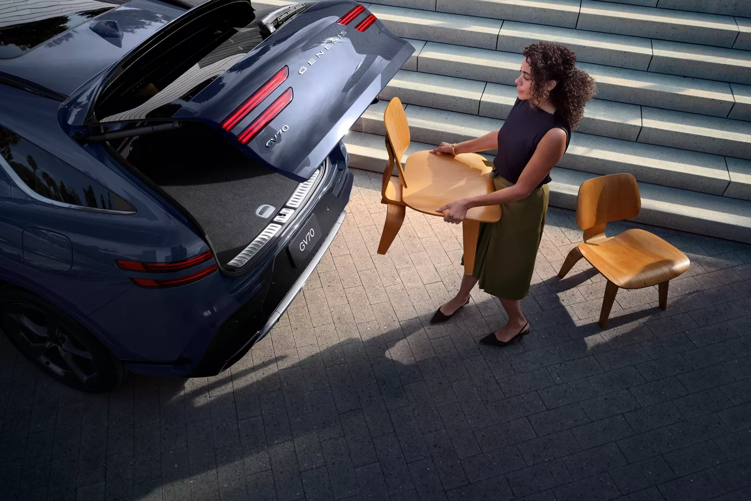3/4 rear overhead driver side view of woman loading chairs into trunk of Genesis GV70