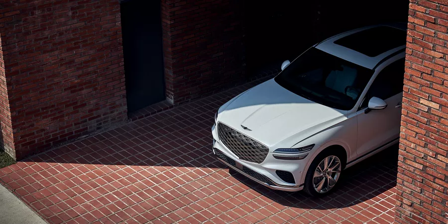 Front aerial view of a Uyuni White Genesis GV70 peaking out of from the corner of a brick wall