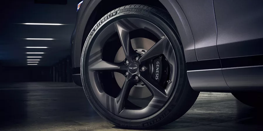 Low-angle close-up of front driver-side wheel and brakes on 2026 Genesis GV70 in Ceres Blue