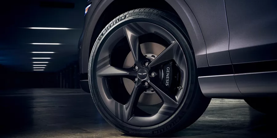 Low angle close-up of Genesis GV70 front driver side wheel, "Genesis" on brake pad