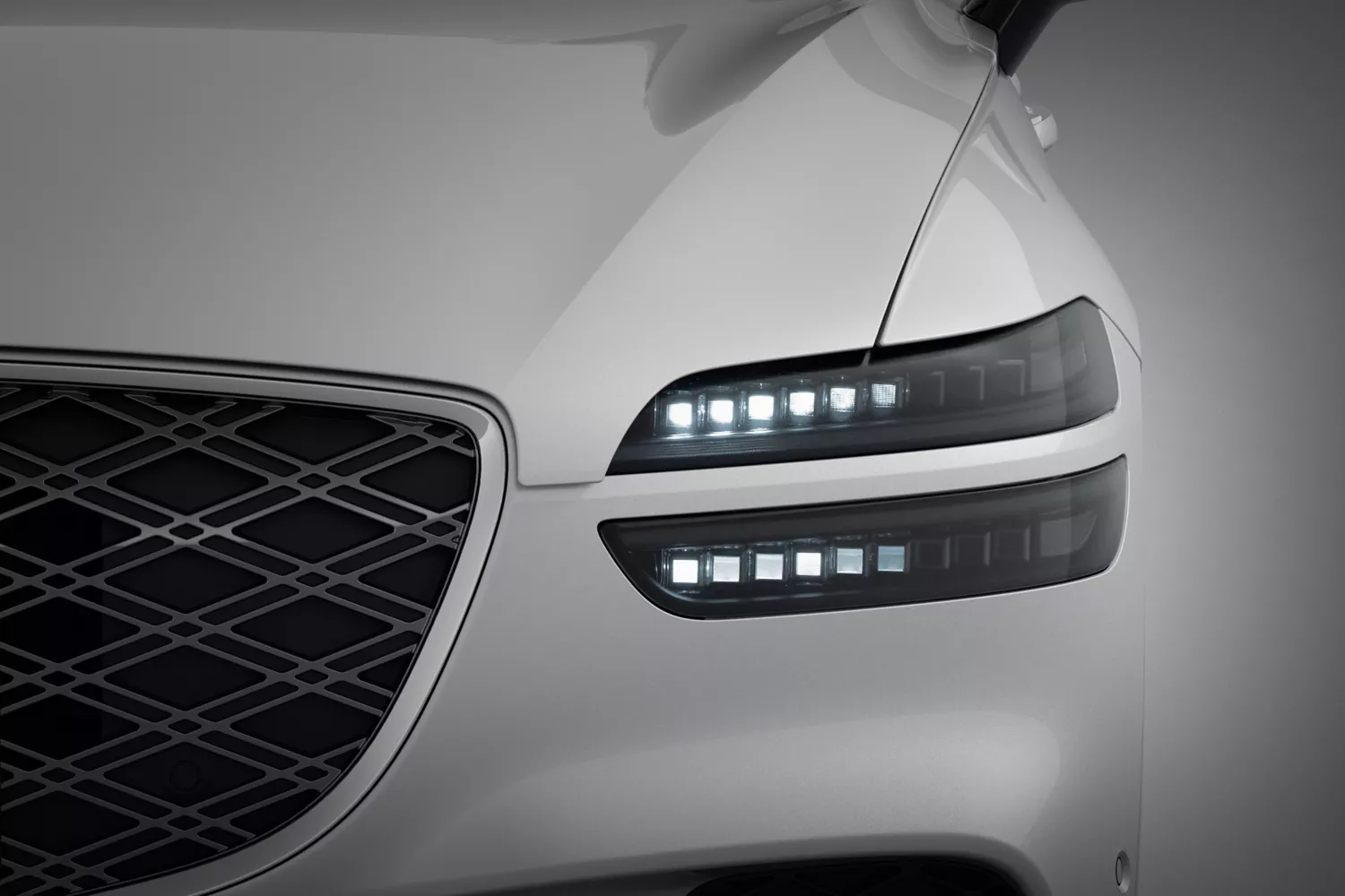 Close-up of front driver side head light and grille on white Genesis GV70