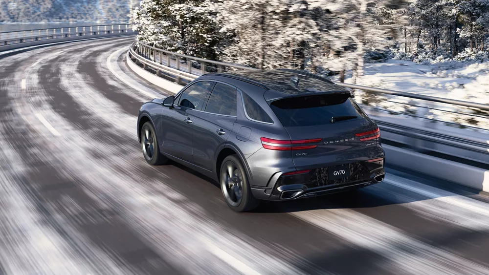 3/4 rear driver side view of Genesis GV70 driving on curved snowy mountainous road