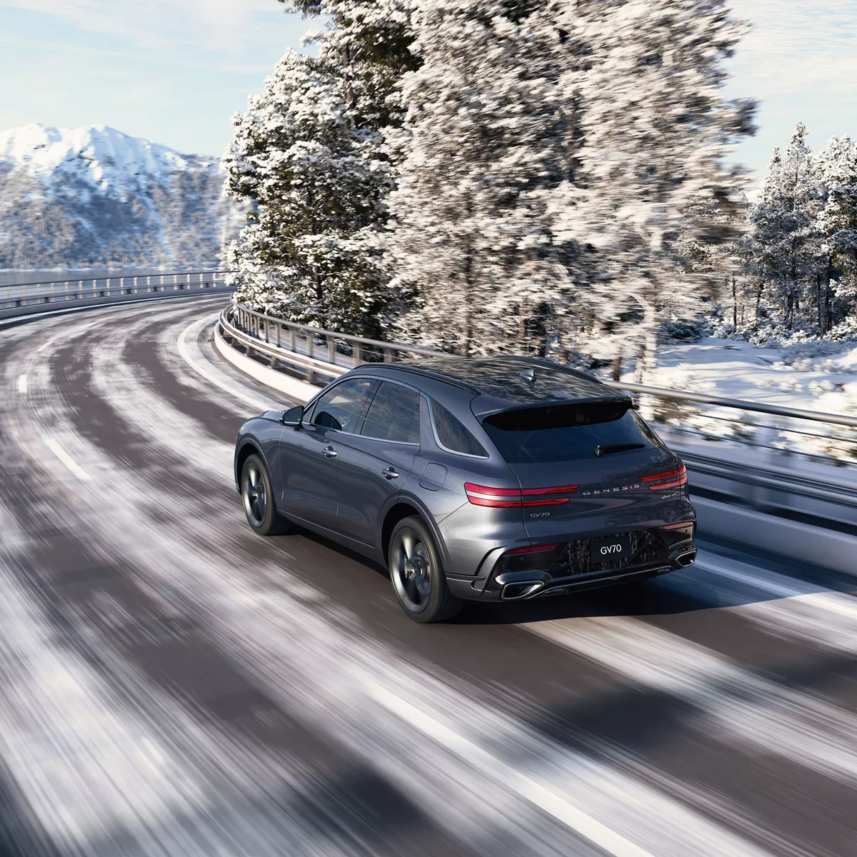 3/4 rear driver side view of Genesis GV70 driving along snowy tree-lined highway