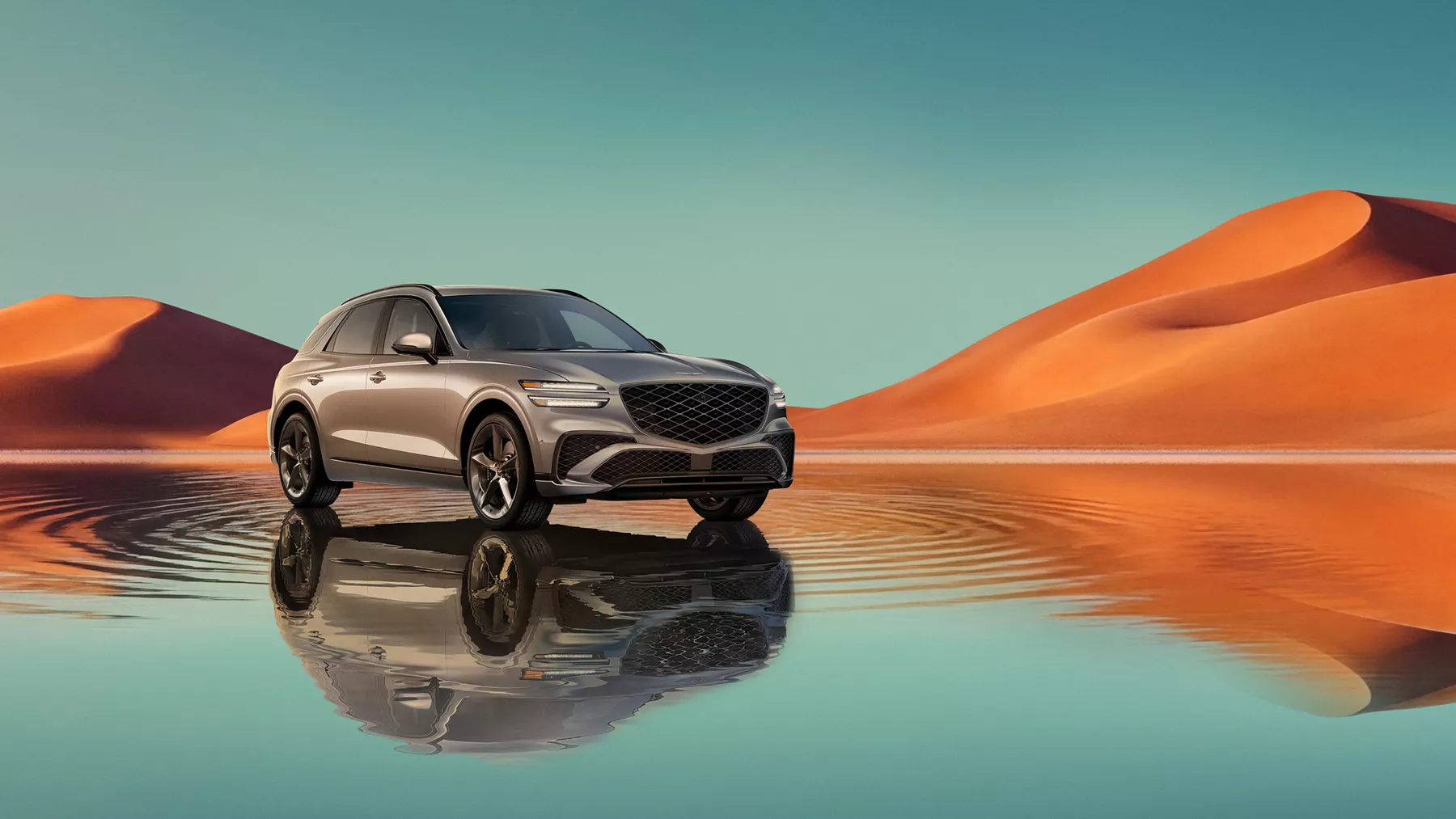 7/8 front passenger view of Savile Silver Genesis GV70 on blue lake w/ orange mountain in background
