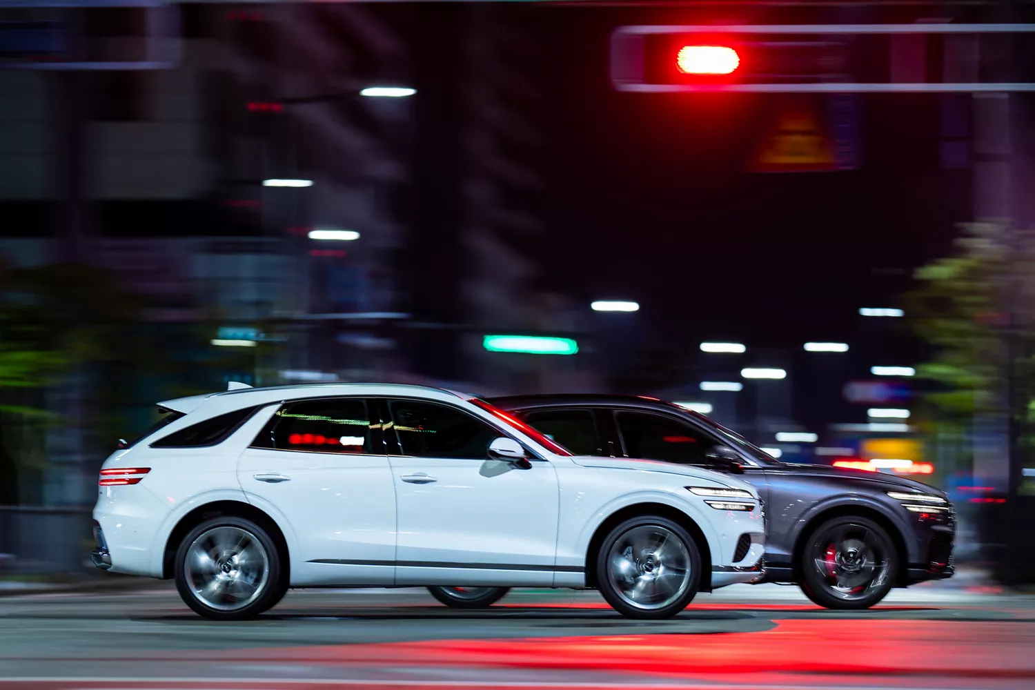 Passenger side profile photo of a Genesis Electrified GV70 in motion, speeding down a city block