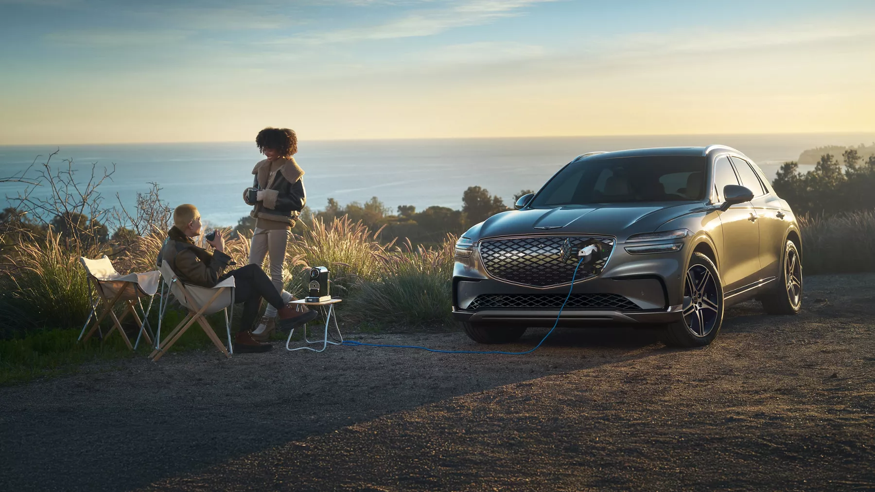 3/4 front view of Genesis Electrified GV70 charging at coastal overlook at sunset