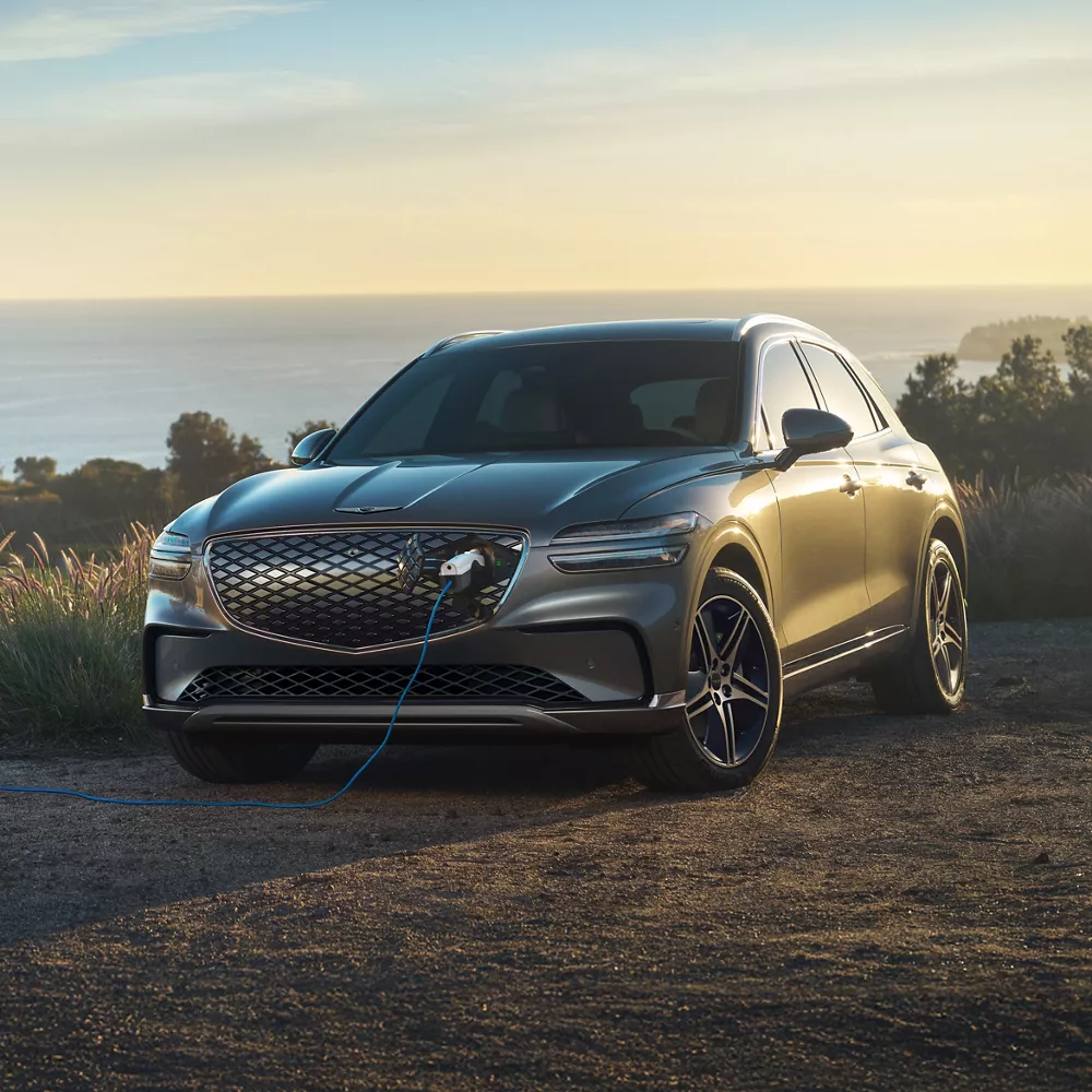 3/4 front view of Genesis Electrified GV70 charging at coastal overlook at sunset