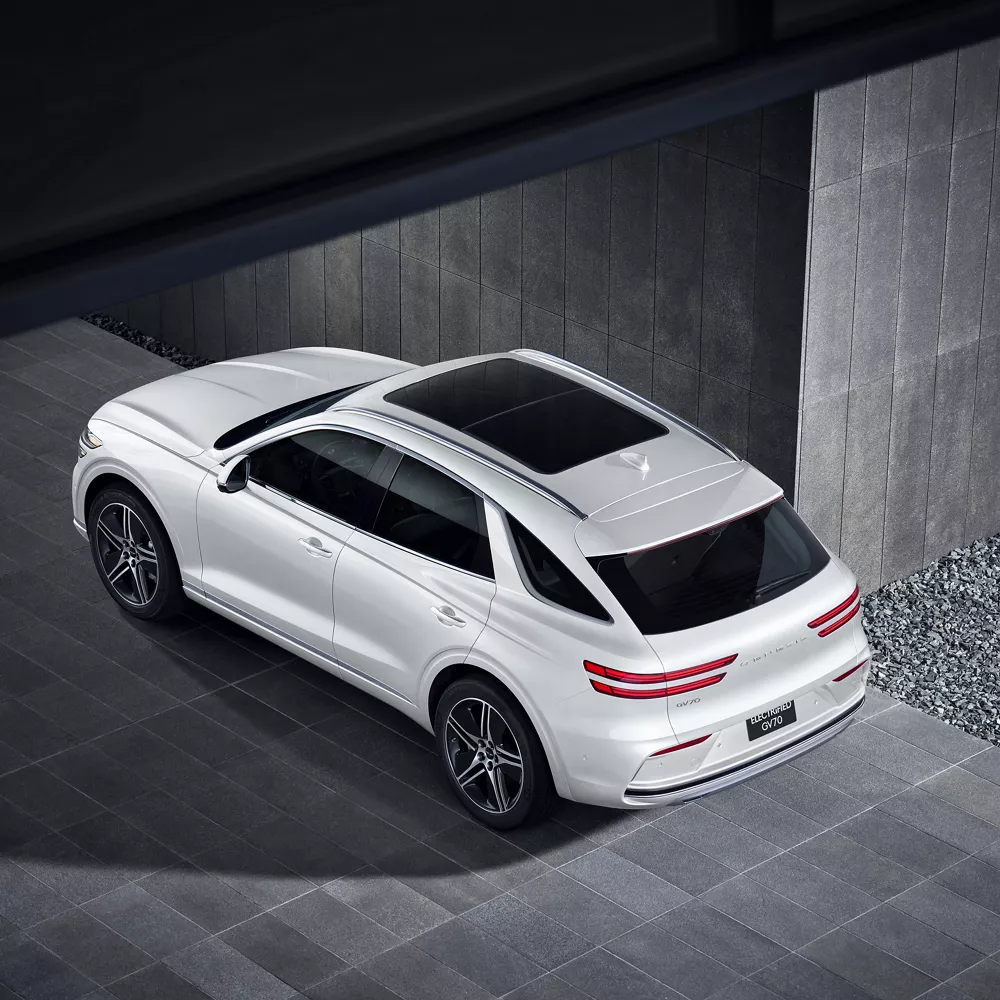 Aerial rear driver side 3/4 view of Genesis Electrified GV70 in Uyuni White parked near a modern building