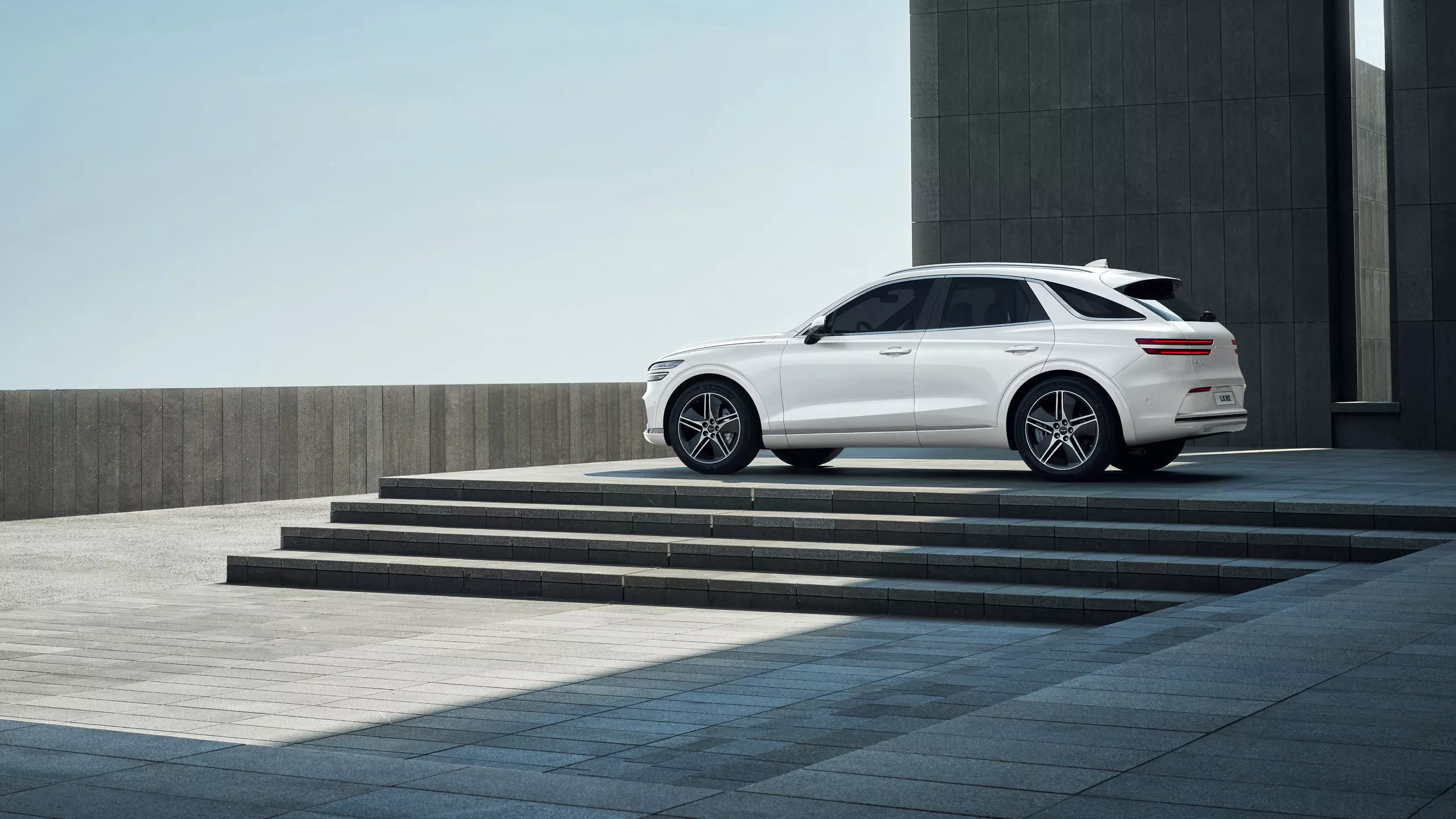 Driver side profile view of Genesis Electrified GV70 in Uyuni White parked near a modern building