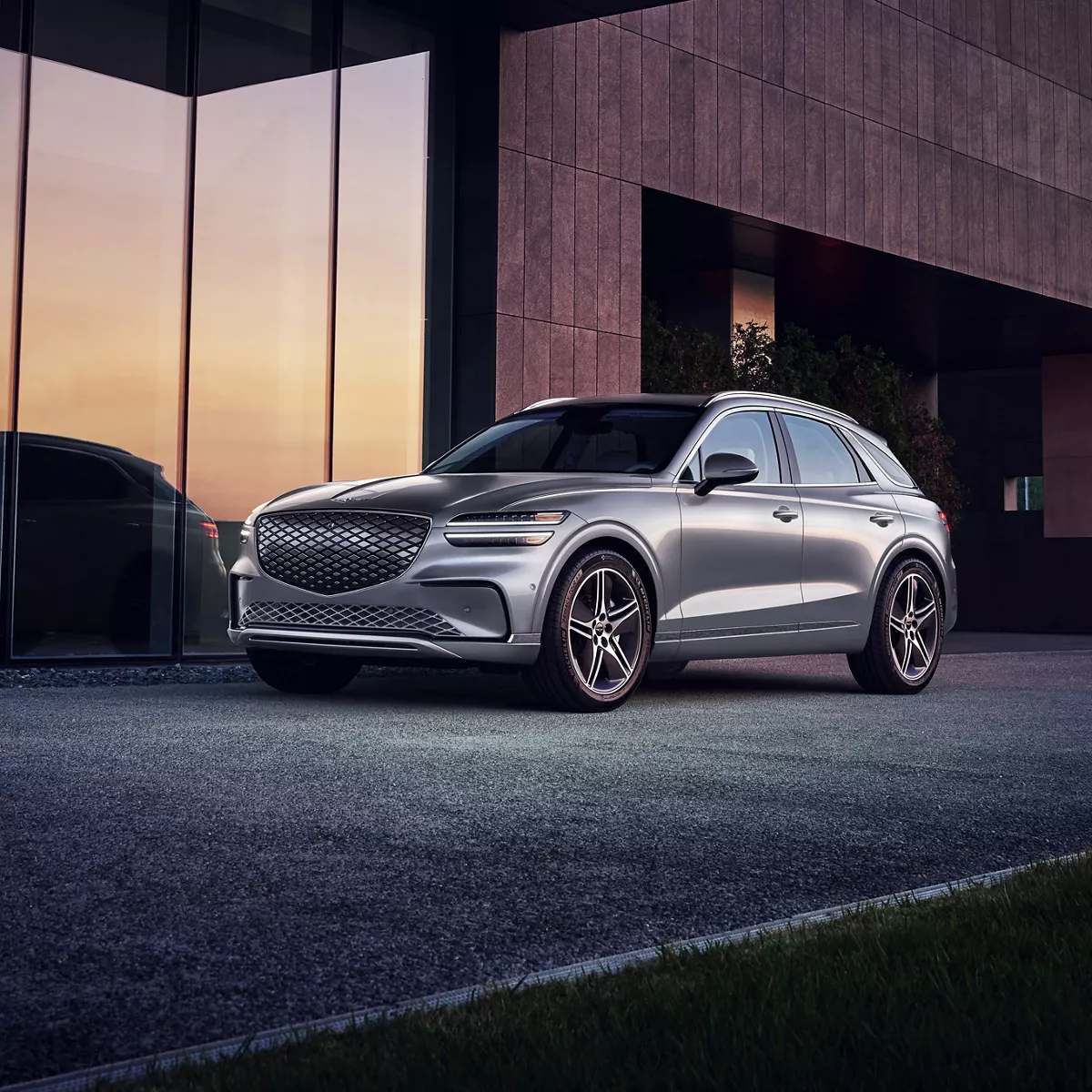 3/4 front driver side view of Genesis Electrified GV70 in Ceres Blue parked beside modern house