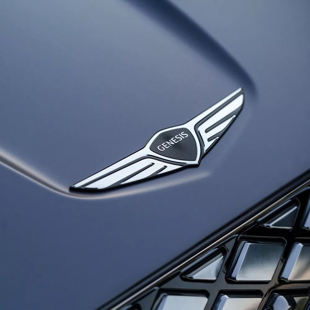 Close up of grille and Genesis emblem on the hood of Genesis Electrified GV70 in Ceres Blue