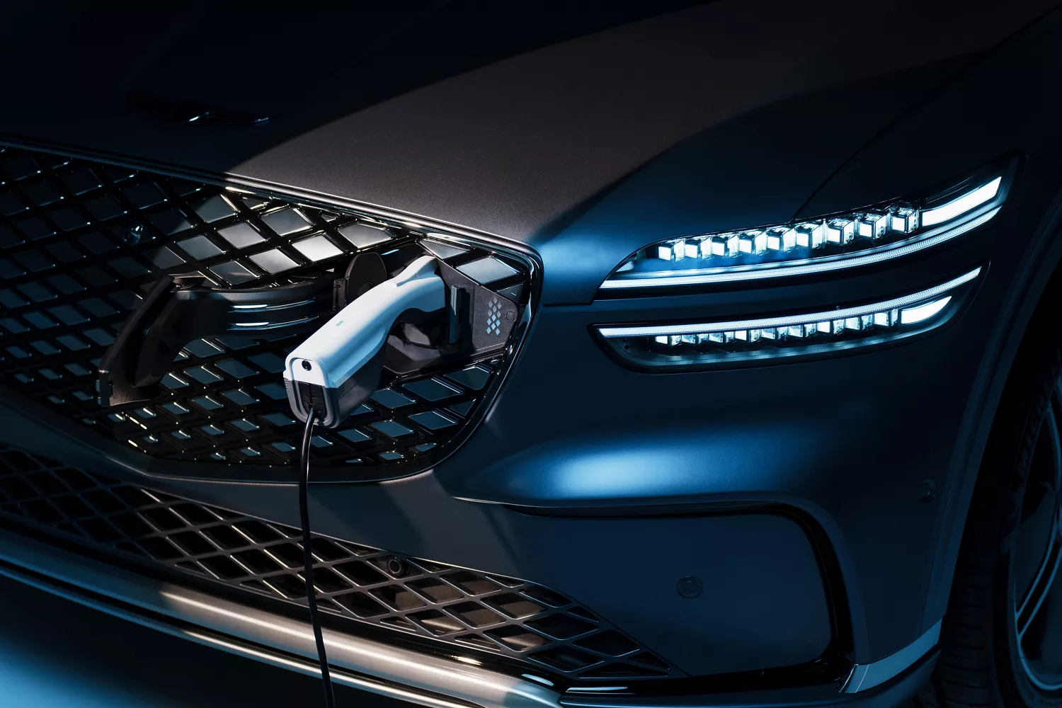 Close up of charger plugged into charge port on the grille of Ceres Blue Genesis Electrified GV70