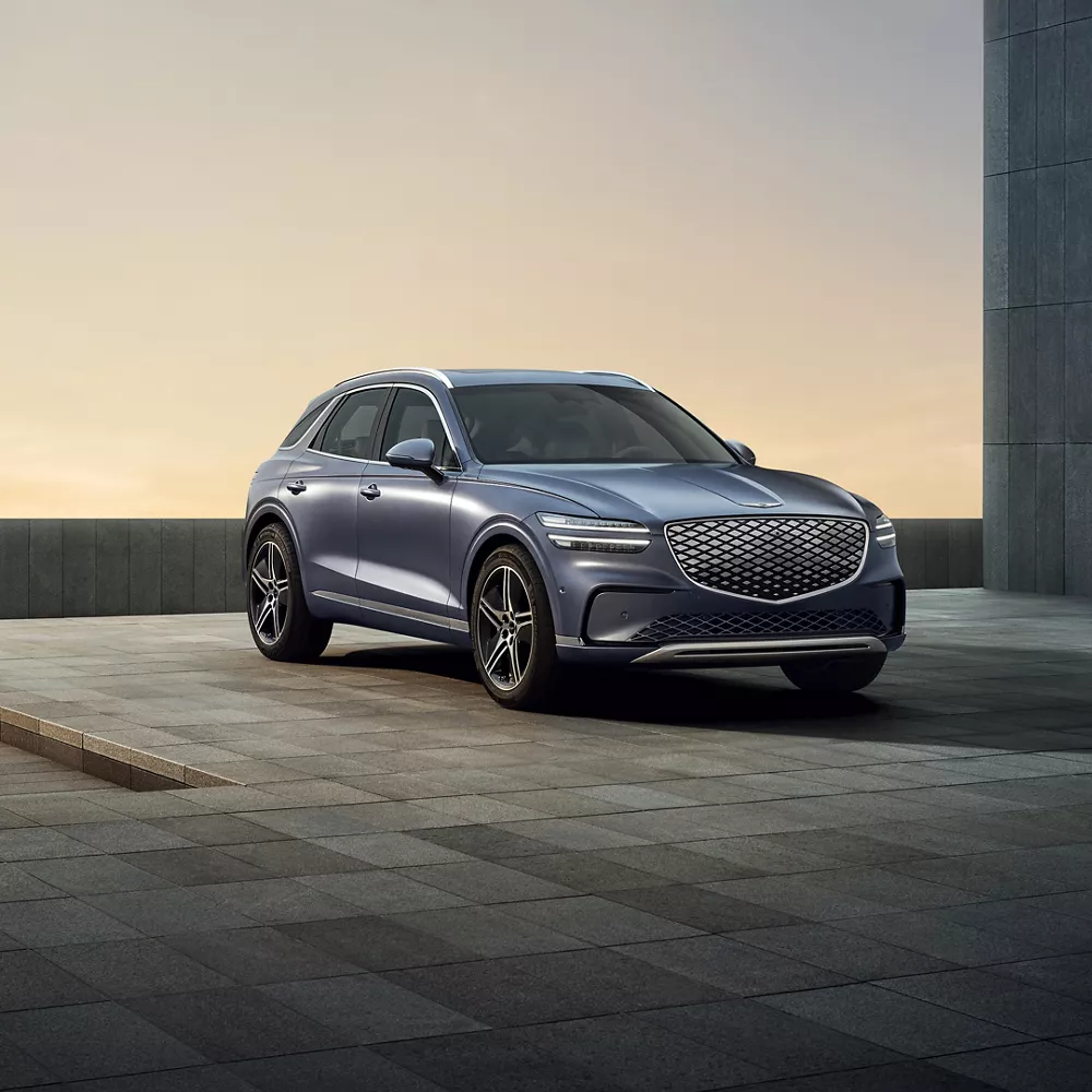 3/4 front passenger side view of Genesis Electrified GV70 in Ceres Blue parked by a modern house