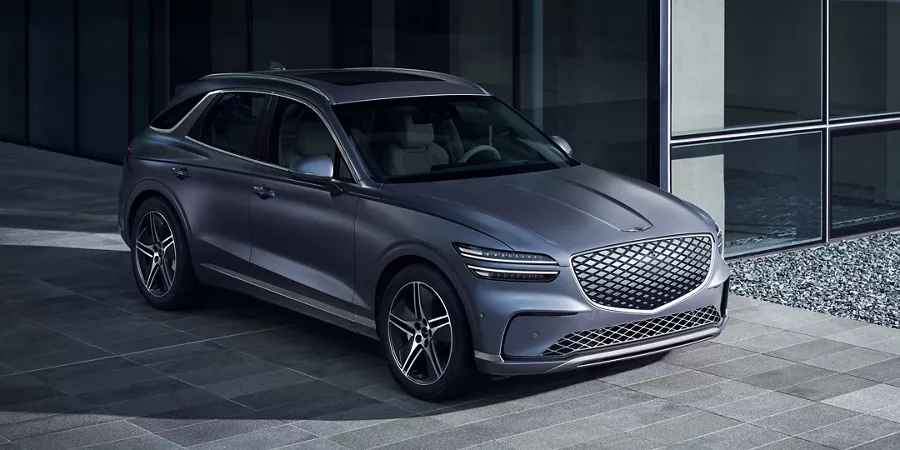 3/4 front passenger side view of Genesis Electrified GV70 in Ceres Blue parked by a modern house