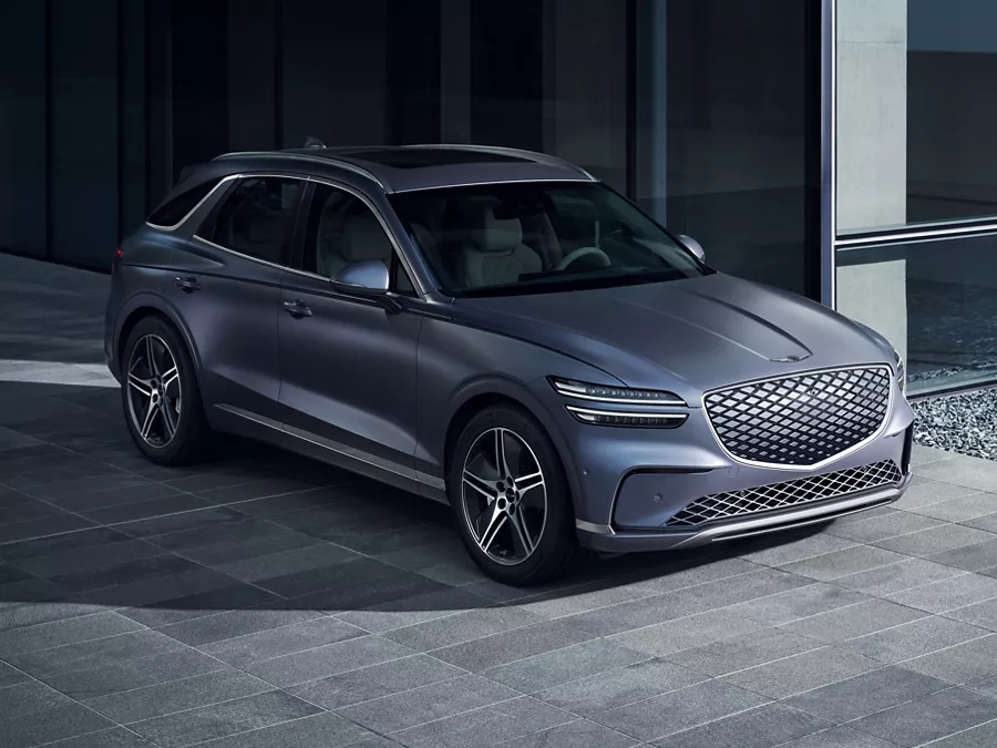 3/4 front passenger side view of Genesis Electrified GV70 in Ceres Blue parked by a modern house