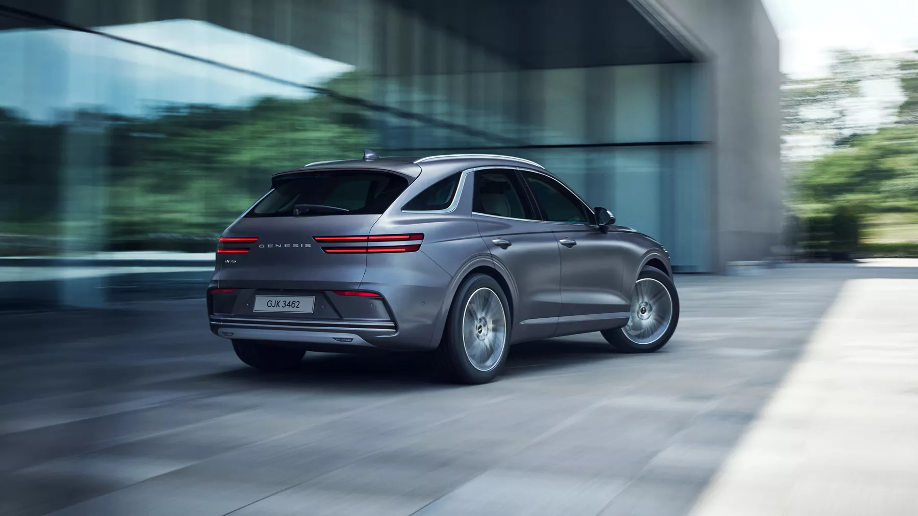 3/4 rear passenger side view of motion blurred Genesis Electrified GV70 in Ceres Blue parked near modern house