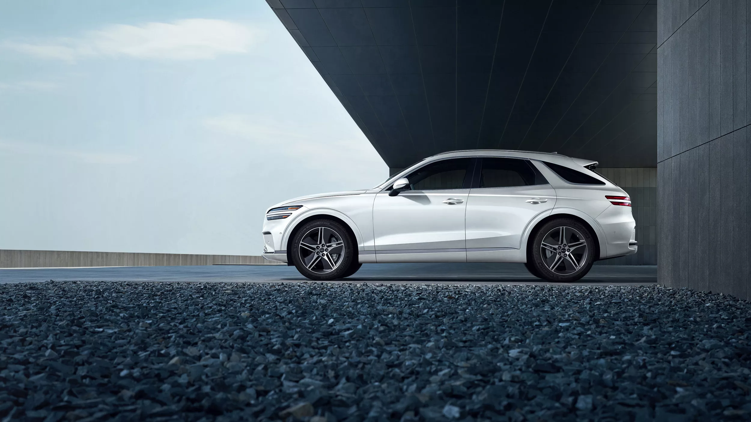 Driver side profile image of Genesis Electrified GV70 in Uyuni White parked in front of modern building