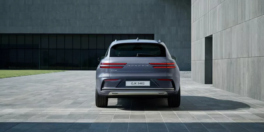 Rear view of Genesis Electrified GV70 in Ceres Blue parked in front of a modern house