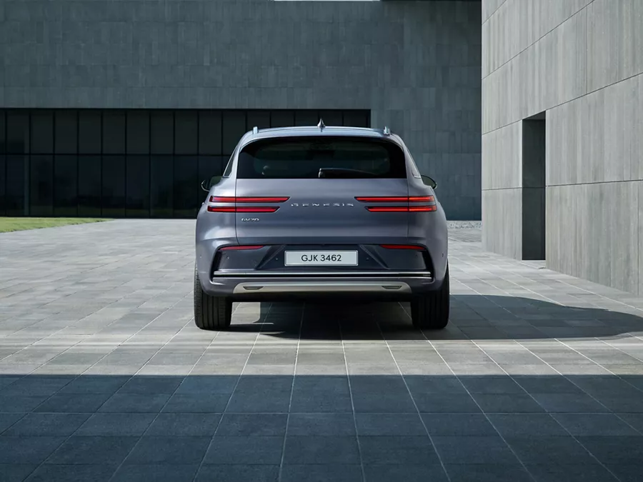 Rear view of Genesis Electrified GV70 in Ceres Blue parked in front of a modern house