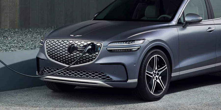 Front driver side view of Genesis Electrified GV70 connected to rapid charger through the grill