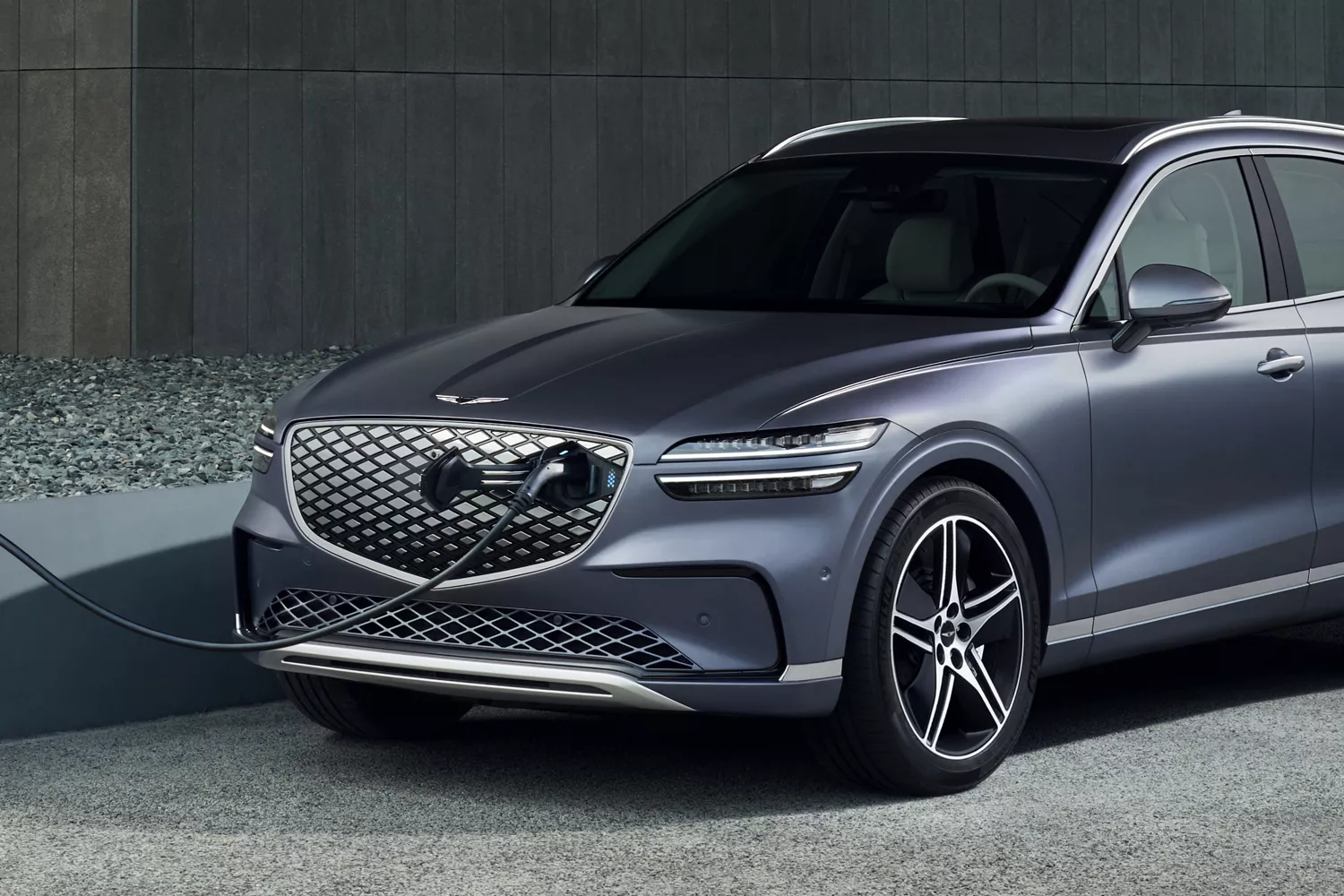 Front driver side view of Genesis Electrified GV70 connected to rapid charger through the grill