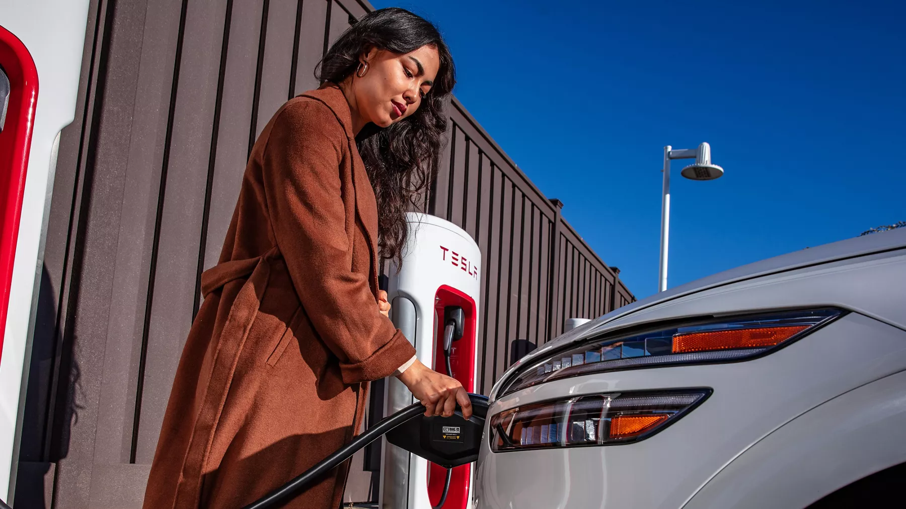 Close up of woman charging a white 2026 Electrified GV70 using the the North American Charging System